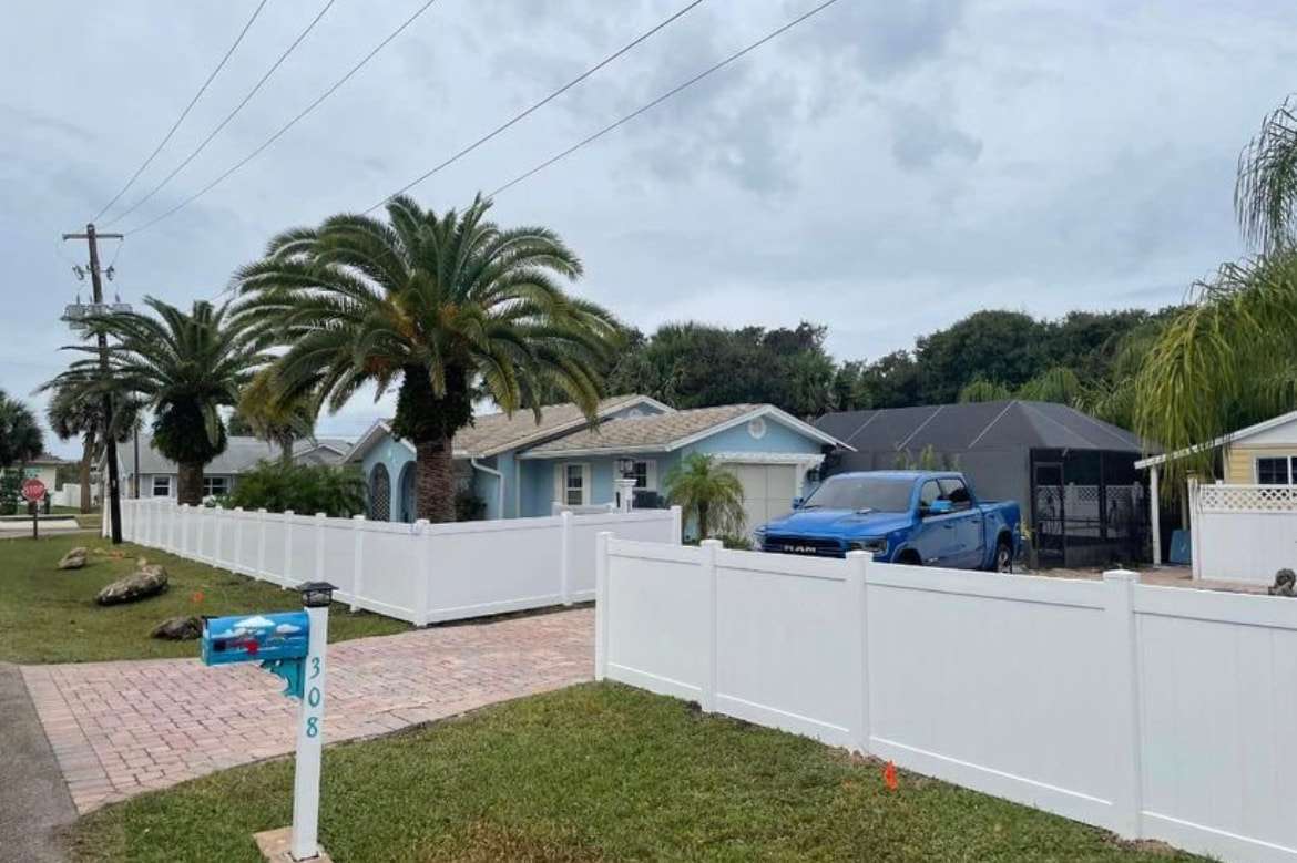 White vinyl fence in a green backyard with a young tree, installed by Lex Fencing